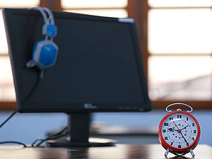 Ein analoger roter Wecker steht vor einem Laptop, an dem ein Kopfhörer hängt