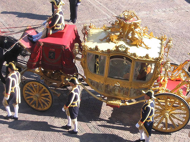 Eine goldene Kutsche wird von Dienern in Livree begleitet.