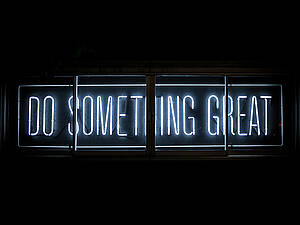 An einer schwarzen Wand prangt eine Leuchttafel mit der Aufschrift "Do something great"... Mach etwas großartiges!