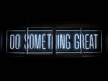 An einer schwarzen Wand prangt eine Leuchttafel mit der Aufschrift "Do something great"... Mach etwas großartiges!