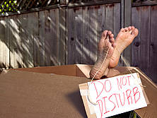 Aus einem großen, braunen Karton schaut ein Fuß heraus. An dessen großer Zehe hängt ein Schild mit der Aufschrift "do not disturb"