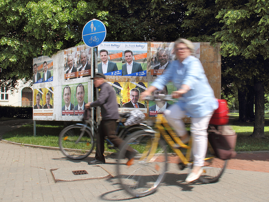 Bürgermeisterwahlen: das OB Konzept - Radfahrer vor einer Plakatwand mit vielen Wahlplakaten in Aalen 2013